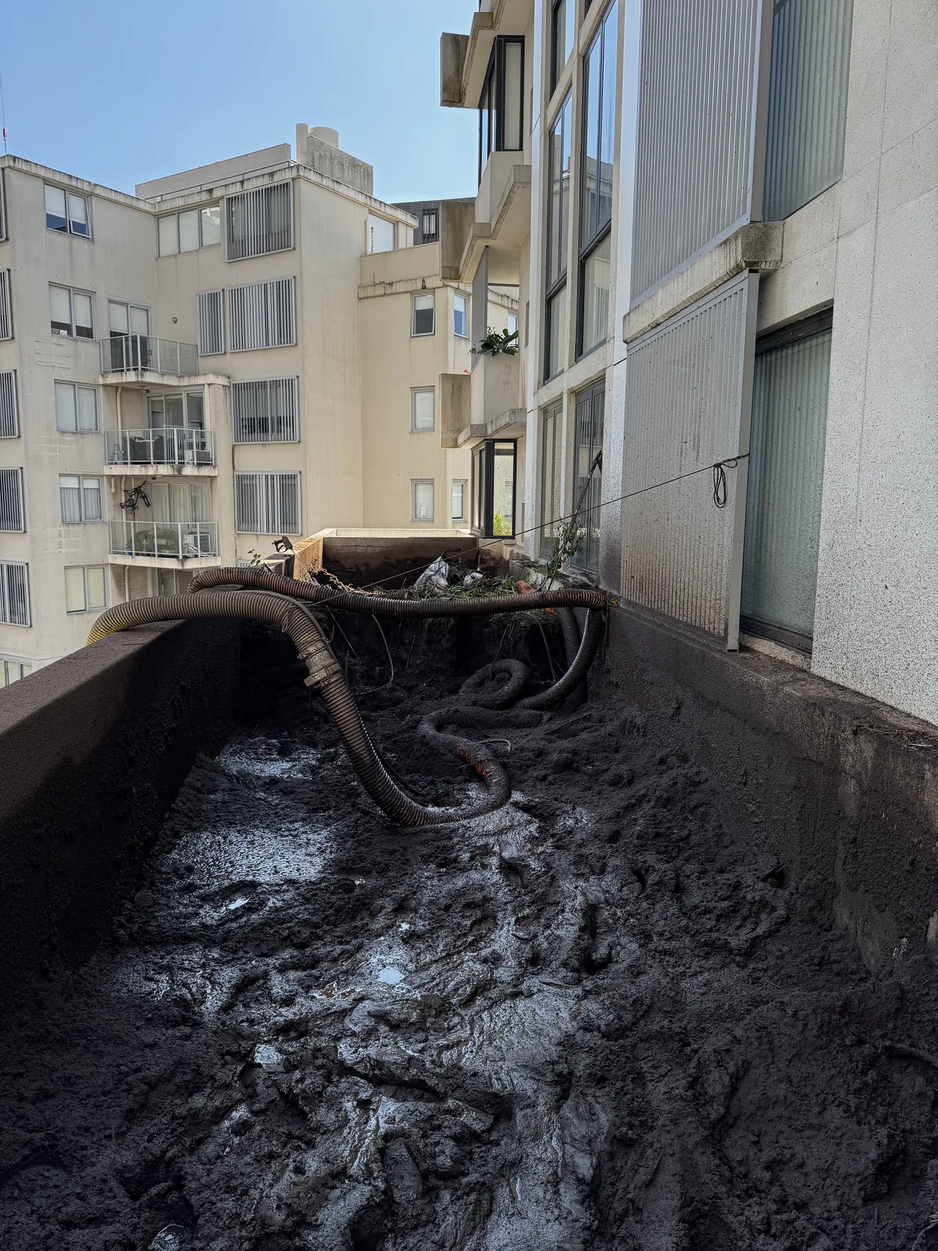 Vac truck hose removing soil and slurry from a high-rise planter box