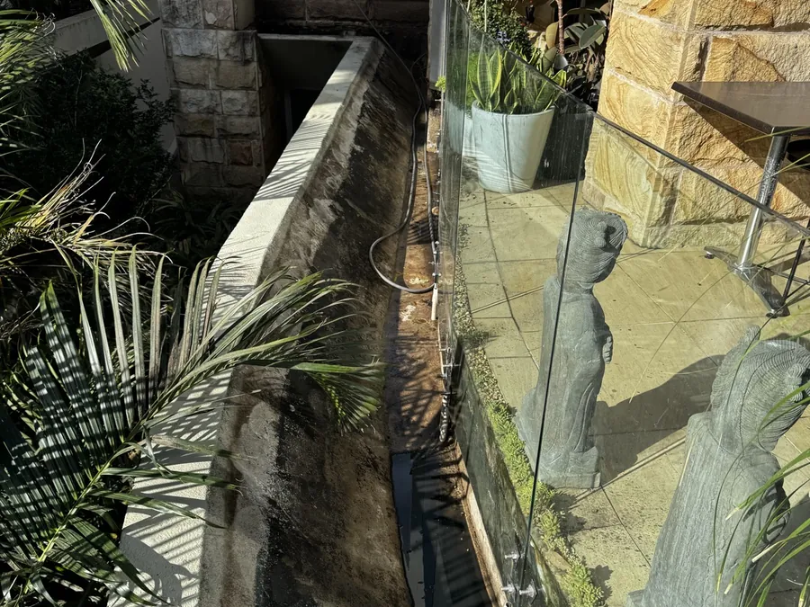 Narrow trench beside a wall with a hose